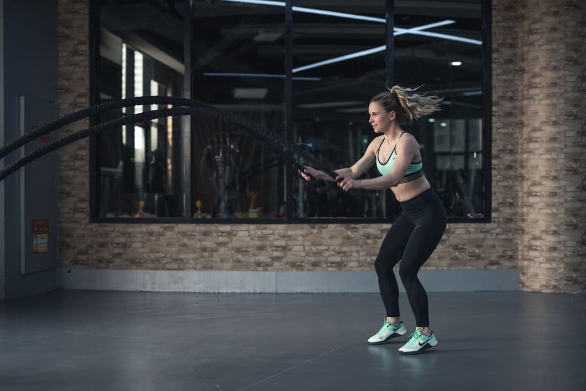 A slim woman training with battle ropes in a gym