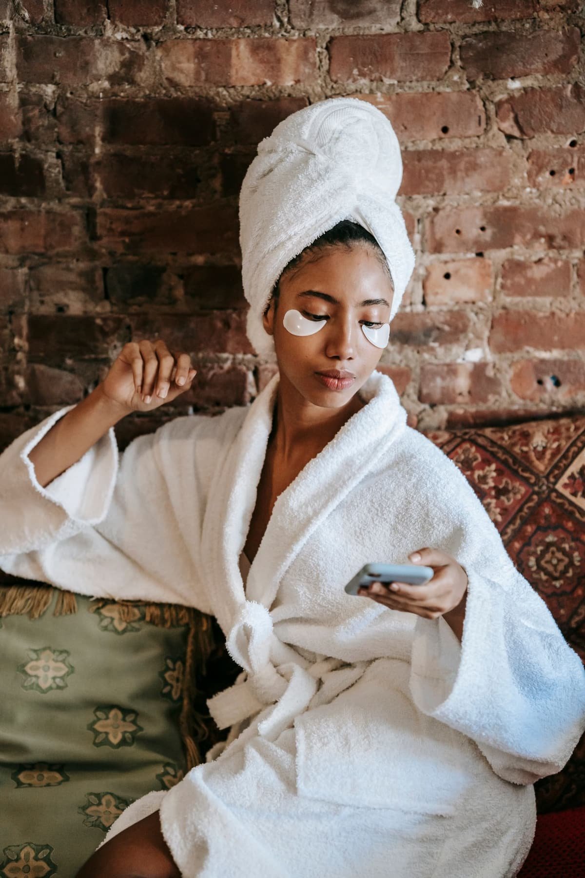 A woman in a bathrobe and hair towel wearing under-eye patches