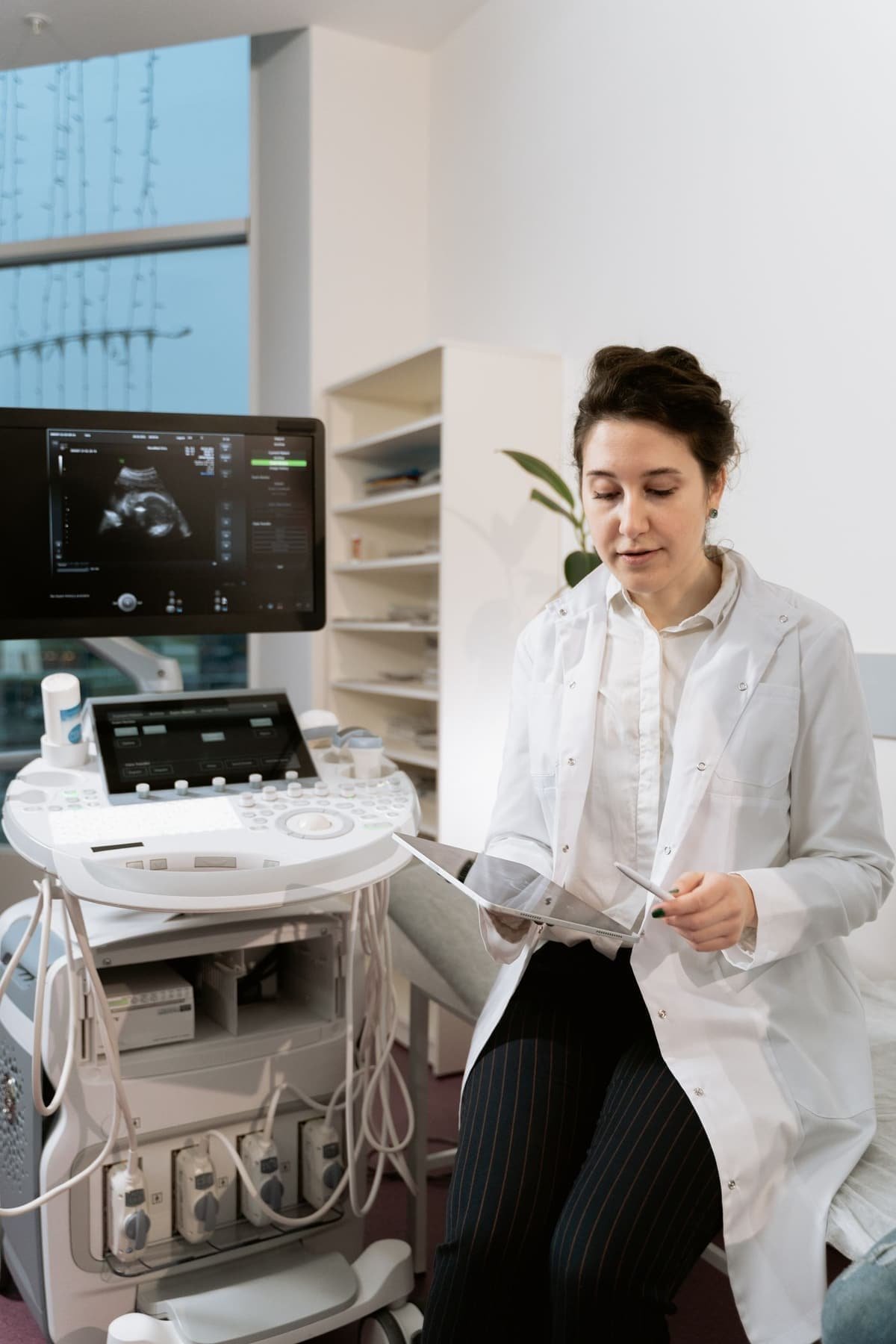 A gynaecologist reads notes beside an ultrasound machine
