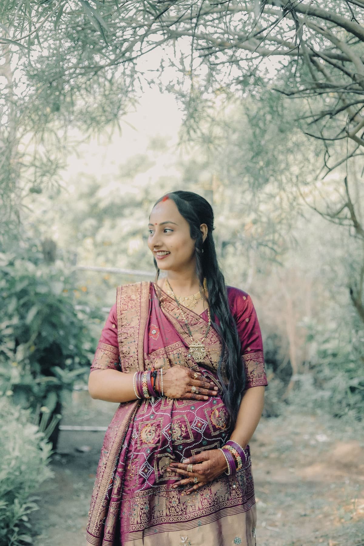 A pregnant Indian woman in a saree, smiling, with her hand on her belly