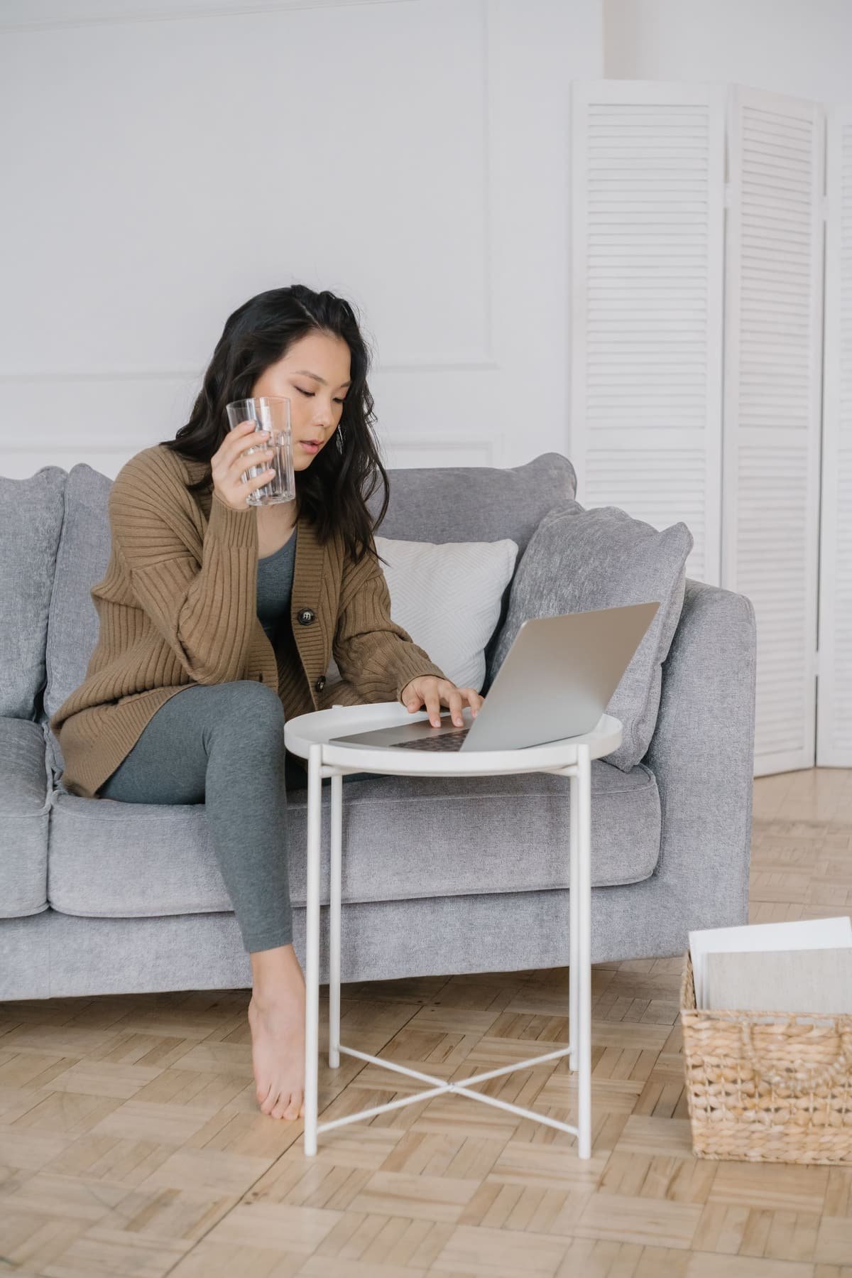 A woman on a sofa with a glass of water, looking at her laptop