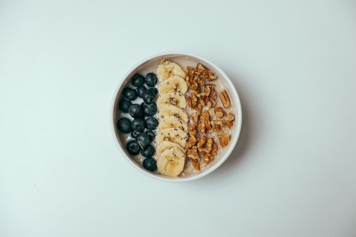A bowl of nuts, banana slices and blueberries