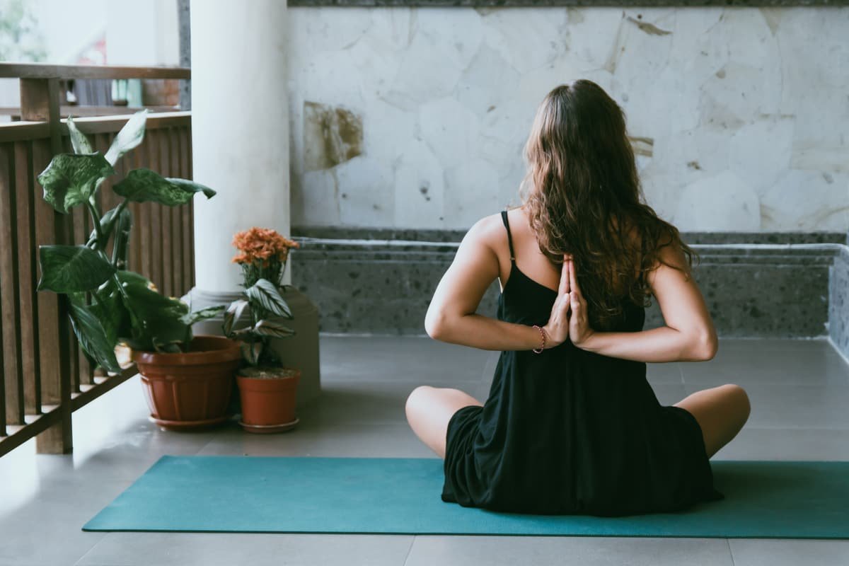 A woman meditating cross-legged on a yoga mat on her balcony