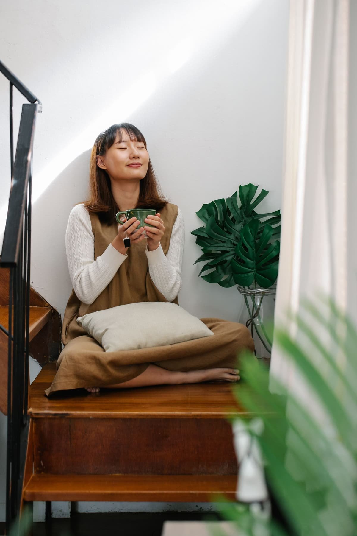 A woman with her eyes closed, holding a cup of tea at home
