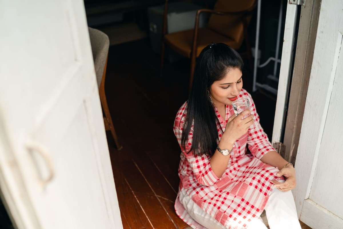 A young Indian woman sipping water by a doorway at home