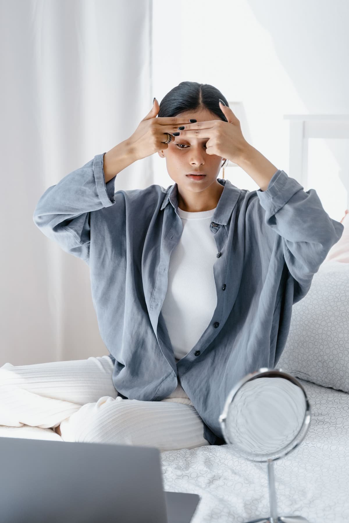 A young woman pressing her fingertips to her forehead and hairline