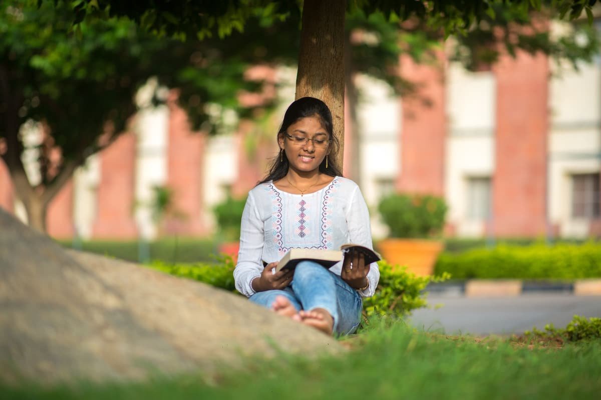 A young Indian college student reading on the grass on campus