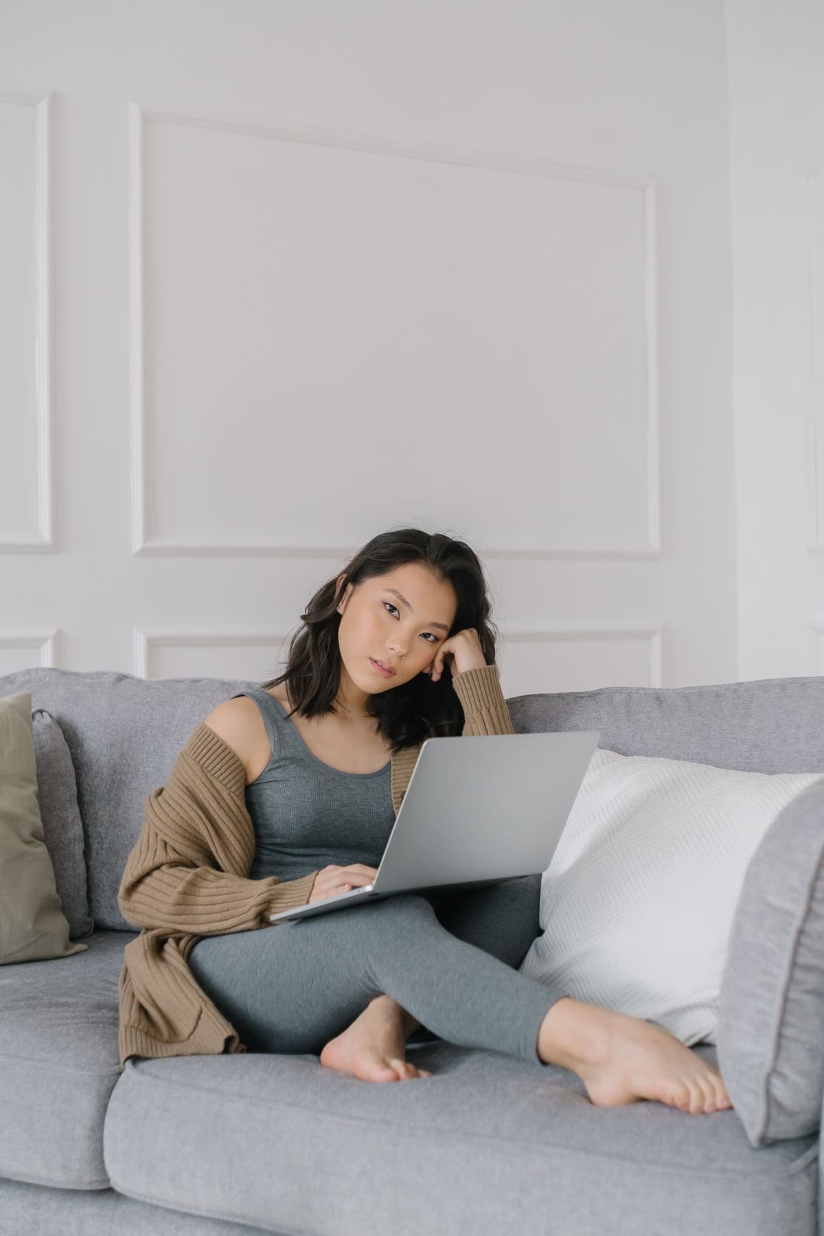 A woman on a sofa with her laptop, thinking