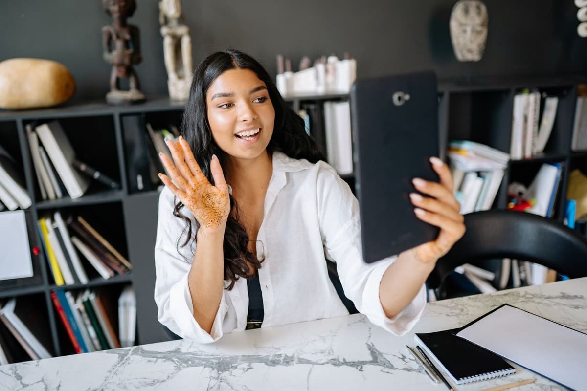A smiling woman waving during a video call at her desk