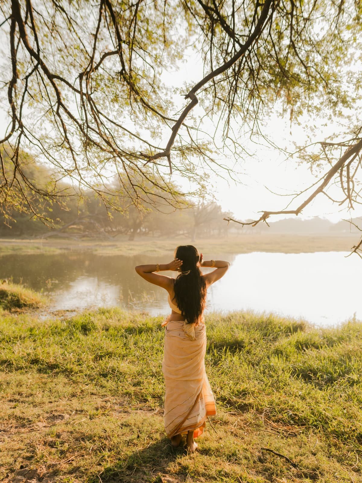A woman standing by a lake under a tree in golden light