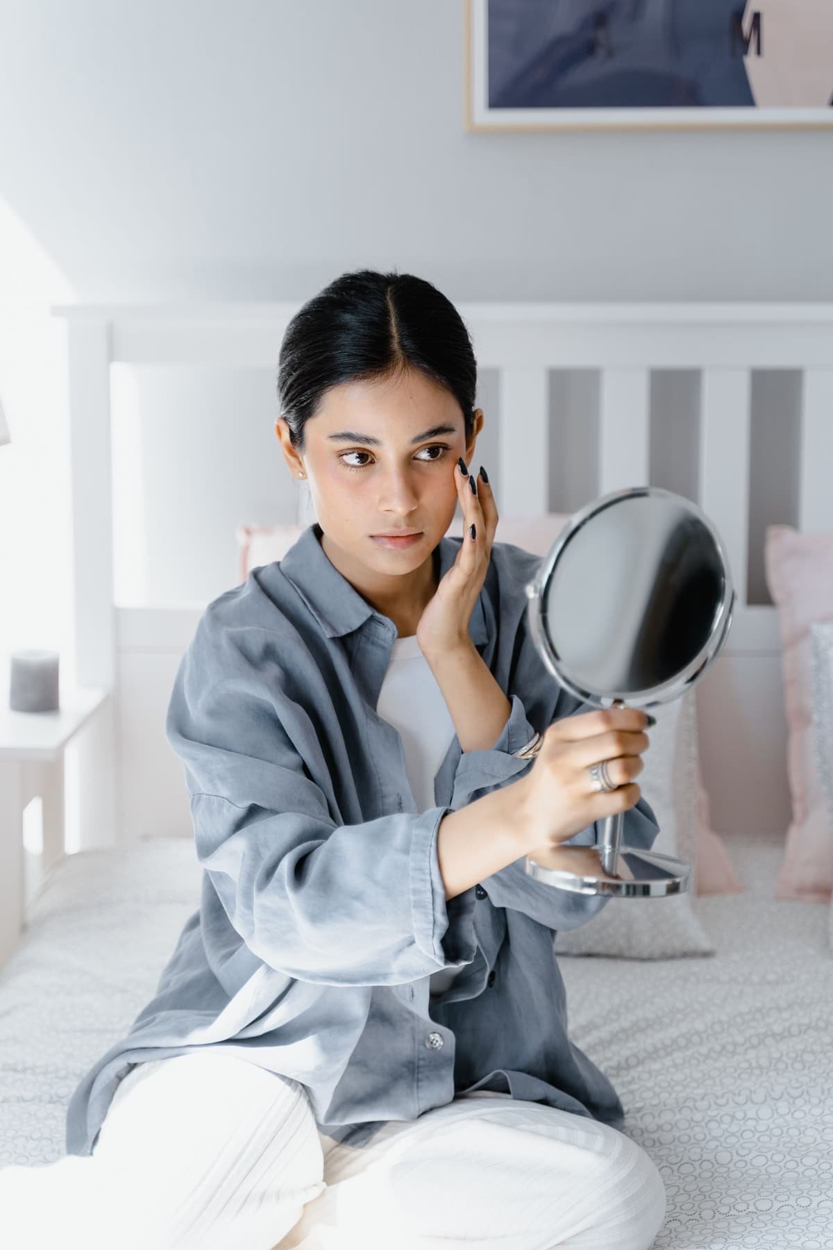 A young woman looking closely at her face in a hand mirror