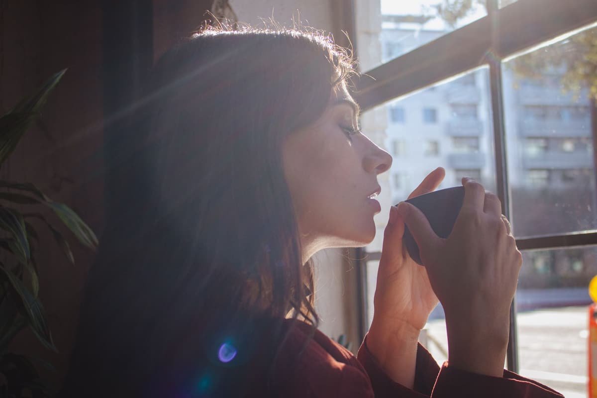 A woman sipping from a mug by a sunlit window