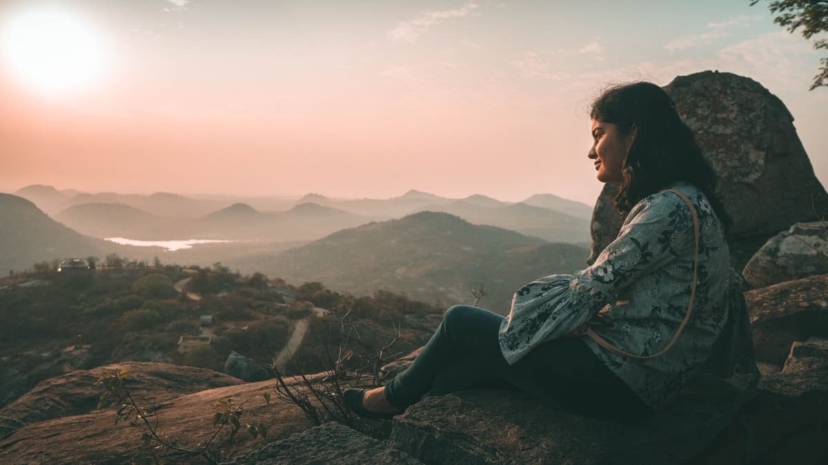 A woman sitting on a rock, looking out over hills at sunrise