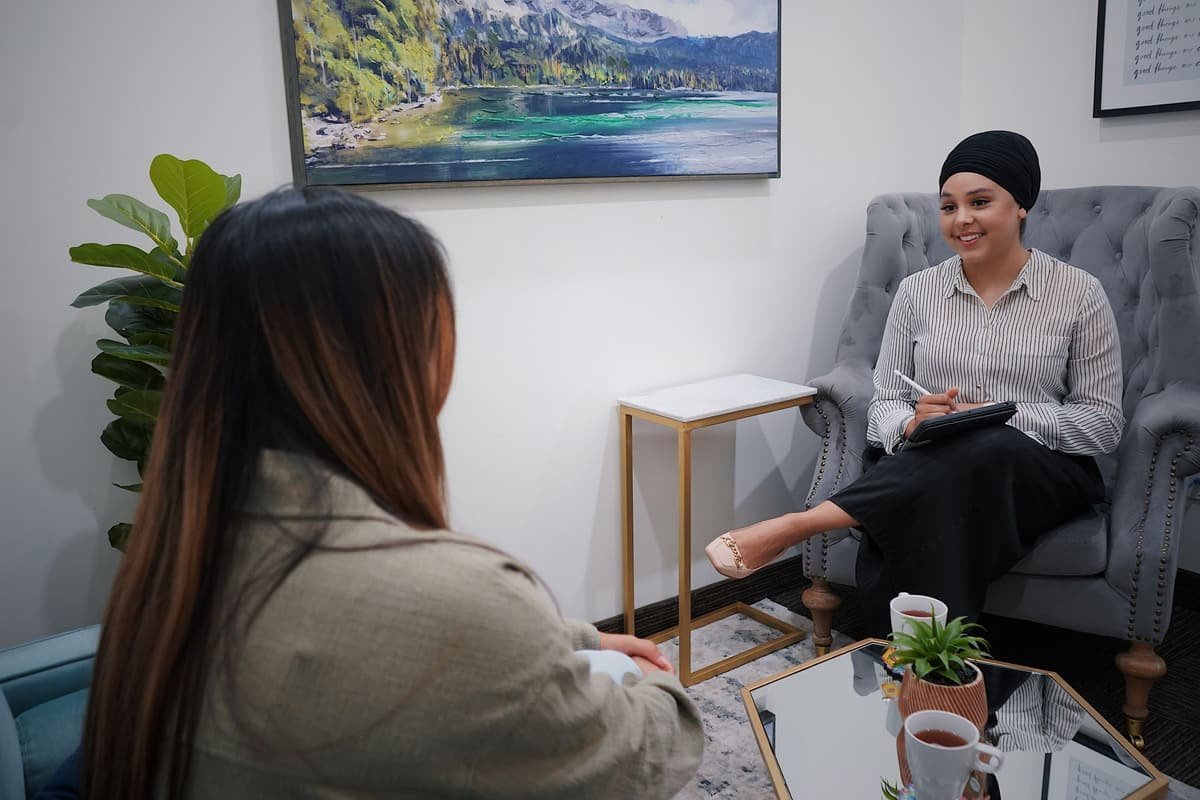 A counselling psychologist smiling and taking notes as a young woman talks with her in a calm, bright room