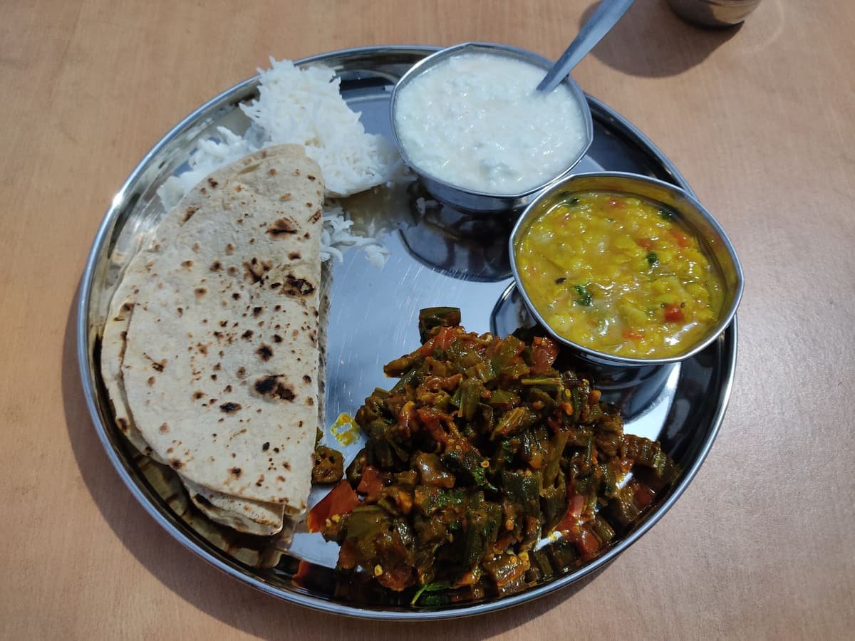 A home-cooked Indian thali on a steel plate with chapati, dal, bhindi sabzi, curd and a little rice